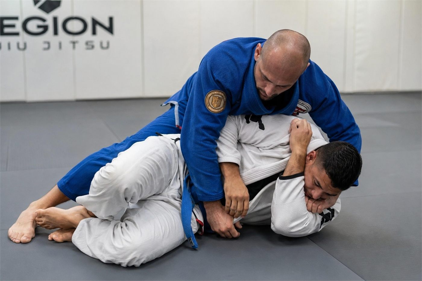 Two students training in the gi, one controlling from the top.