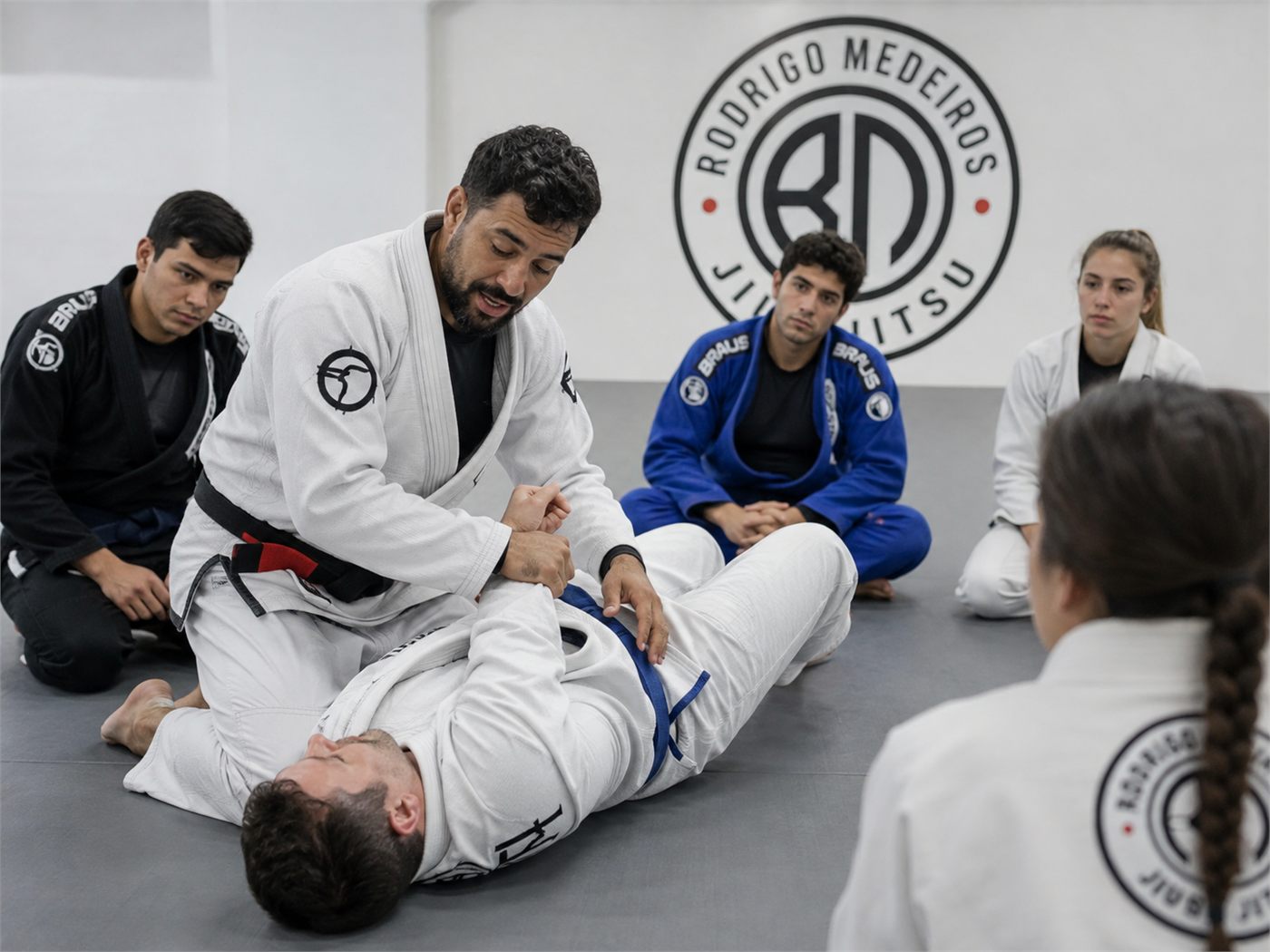 An instructor demonstrating a technique while the class watches from the mat.