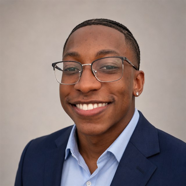 Eddy Ramos, smiling, wearing glasses and a navy jacket over a light blue shirt.
